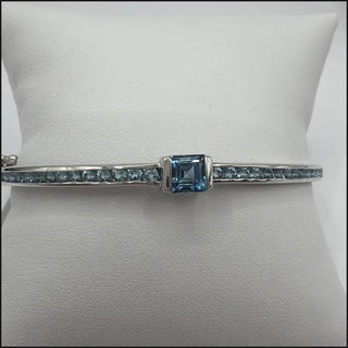 Sterling silver blue topaz bangle with square center stone and channel-set side stones